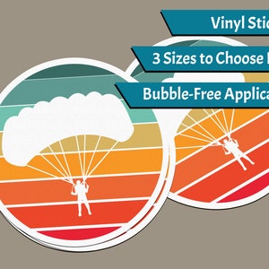 Puede incluir: Un conjunto de tres pegatinas redondas de vinilo que presentan una silueta de una persona haciendo paracaidismo con un paracaídas sobre un fondo de puesta de sol retro colorido. Las pegatinas están disponibles en tres tamaños y tienen una aplicación sin burbujas.