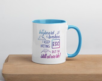 May include: White ceramic mug with a light blue rim and handle. The mug has a humorous message that reads "My keyboard is broken. I keep hitting ESC but I'm still at work!"