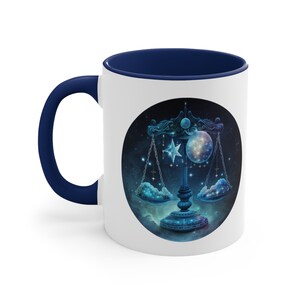 May include: White ceramic mug with a navy blue handle and interior. The mug features a celestial design of a scale, star, and moon against a starry background. The design is in shades of blue, teal, and white.