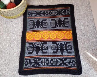 May include: A black, gray, orange, and green crocheted rug with a geometric pattern. The rug has a black border.