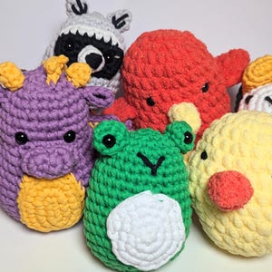 Puede incluir: Colección de peluches de ganchillo hechos a mano con forma de animales. Incluye una abeja amarilla, un dragón morado, una rana verde, un pulpo rojo, un pollito amarillo, un mapache gris y un rollo de sushi. Cada peluche tiene ojos de seguridad negros.