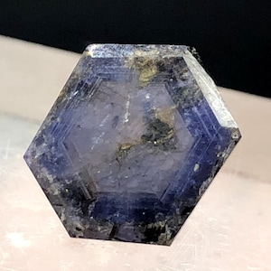 May include: A hexagonal crystal with a deep blue colour, displaying natural mineral formations. The crystal's surface has a textured appearance with darker inclusions and subtle colour variations. The overall shape is symmetrical, with sharp edges and a polished look.