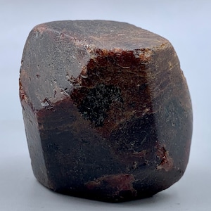 Puede incluir: Una gema facetada, de color marrón rojizo oscuro, con una forma ligeramente irregular. La superficie tiene un aspecto natural y texturizado, con variaciones de color y tono. La gema es probablemente un espécimen mineral, posiblemente un granate.