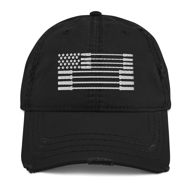May include: Black distressed baseball cap featuring a white embroidered design of the American flag. The flag design is stylized with barbell shapes and stars. The cap has a curved brim and a worn, vintage look.