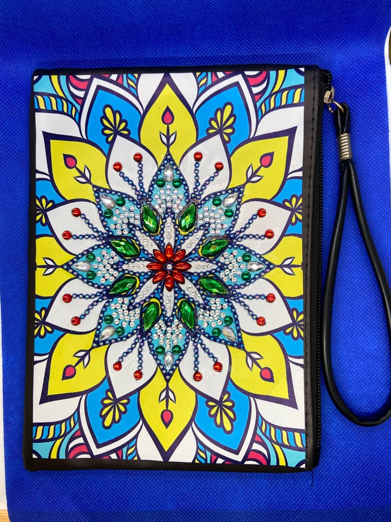May include: A black zippered pouch with a colorful mandala design featuring a central flower with green, blue, and red rhinestones. The pouch has a black strap.