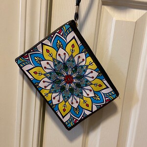 May include: A white zippered pouch with a colorful mandala design featuring blue, yellow, red, and green colors. The mandala has a beaded center with a black border around the pouch.