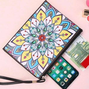 May include: A colorful zippered pouch with a mandala design. The pouch has a black zipper and a black strap. The pouch is open and has a phone and money inside.