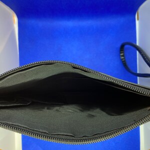 May include: Black zippered pouch with a black strap. The pouch is open and the inside is lined with black fabric.