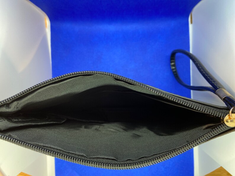 May include: Black zippered pouch with a black strap. The pouch is open and the inside is lined with black fabric.