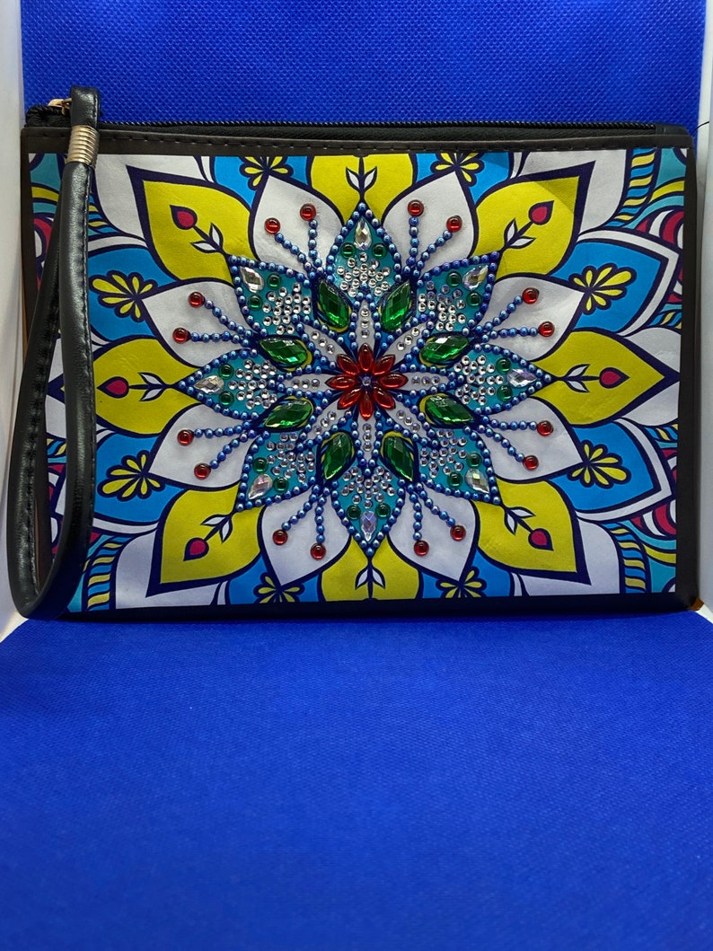 May include: A black zippered pouch with a colorful mandala design featuring a central flower with blue, green, and red rhinestones. The pouch has a black strap.
