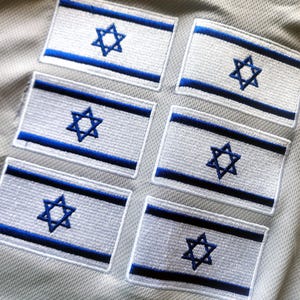 Puede incluir: Seis parches bordados con la bandera de Israel. Cada parche tiene un fondo blanco, una estrella de David azul y rayas azules. Los parches son rectangulares y están dispuestos sobre una superficie texturizada.