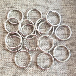 May include: A collection of silver-colored key rings, arranged on a textured, light brown surface. The key rings are circular and appear to be made of metal. The image is well-lit, highlighting the metallic sheen of the rings.
