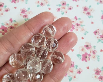 May include: A collection of small, clear, round, faceted glass beads. Each bead features a multi-faceted surface that reflects light, creating a sparkling appearance. The beads are transparent and have a central hole for stringing purposes.