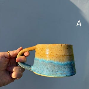 Può includere: Tazza in ceramica fatta a mano con una sfumatura di colore unica. La metà superiore è giallo-arancio caldo, che sfuma in un blu vibrante nella parte inferiore. Dotata di un manico robusto. Un pezzo funzionale e artistico per gustare bevande.