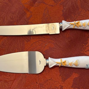 May include: A set of two white and blue cake knives with seashell and starfish designs. The knives have silver blades.