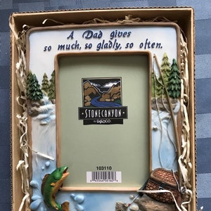 May include: Decorative picture frame with a fishing theme. The frame is white with a light blue border and features a sculpted waterfall, trees, and a fish jumping out of the water. The text reads "A Dad gives so much, so gladly, so often."