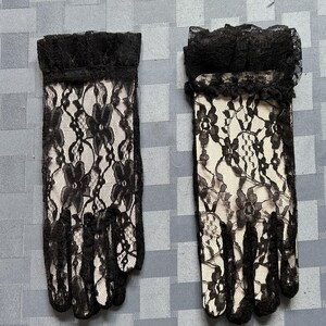 May include: A pair of black lace gloves with a ruffled trim. The gloves are made of delicate lace with a floral pattern.