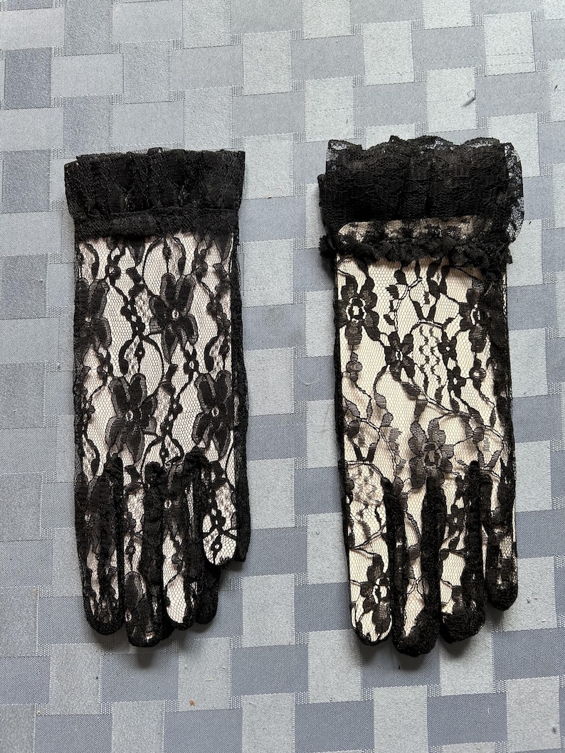 May include: A pair of black lace gloves with a ruffled trim. The gloves are made of delicate lace with a floral pattern.