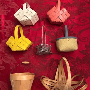 May include: A collection of six small baskets featuring a white square basket, a coral square basket, a yellow square basket, a silver wire basket, a blue and tan woven basket, a light wood bucket with a wire handle, and a natural wood basket.