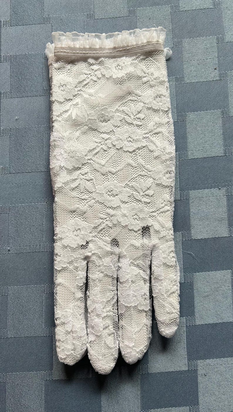 May include: White lace gloves with a delicate floral pattern and a ruffled edge.