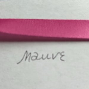 May include: A horizontal strip of bright pink satin ribbon positioned above the handwritten word mauve in dark gray ink on a plain white background. The ribbon has a smooth, reflective texture and spans the width of the frame.