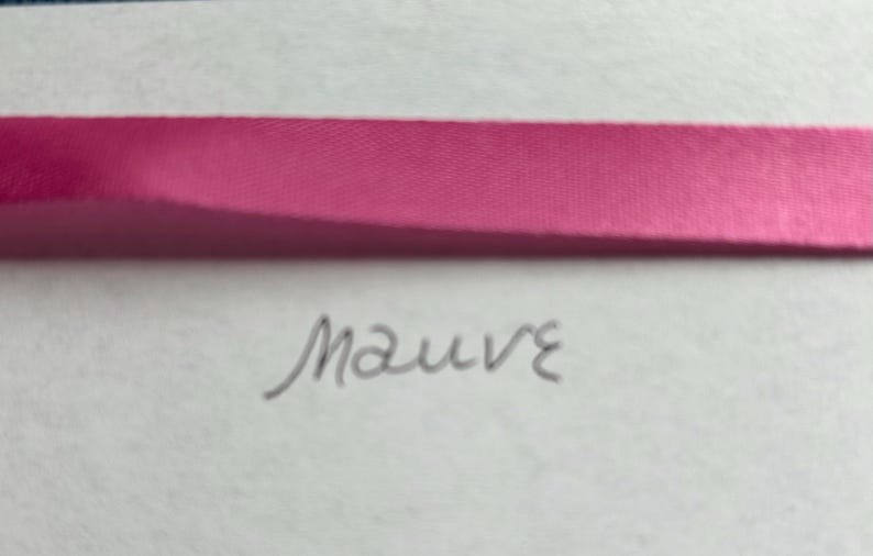May include: A horizontal strip of bright pink satin ribbon positioned above the handwritten word mauve in dark gray ink on a plain white background. The ribbon has a smooth, reflective texture and spans the width of the frame.