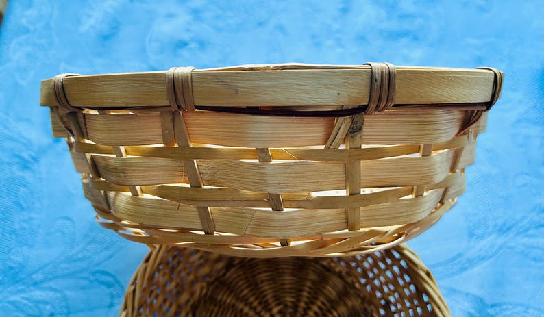 Puede incluir: Una cesta redonda y poco profunda construida con tiras de madera natural de color claro tejidas en un patr&oacute;n horizontal. El borde est&aacute; reforzado con una banda de madera lisa y gruesa asegurada por tiras verticales, creando un recipiente abierto.