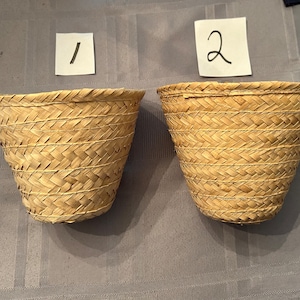 May include: Two woven baskets made of natural materials, labeled 1 and 2. The baskets are light brown and have a conical shape.
