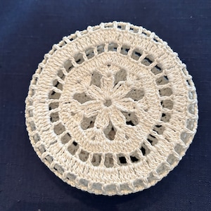 May include: A white crocheted doily with a circular design and a flower in the center.