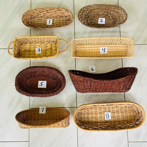 May include: Eight woven baskets of various shapes and sizes, labeled with numbers one through eight. The collection includes oval, rectangular, and curved designs in light tan, medium brown, and dark brown tones, featuring different weave patterns.