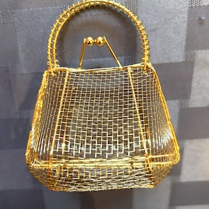 May include: A gold wire mesh handbag with a wire handle and two gold ball accents.