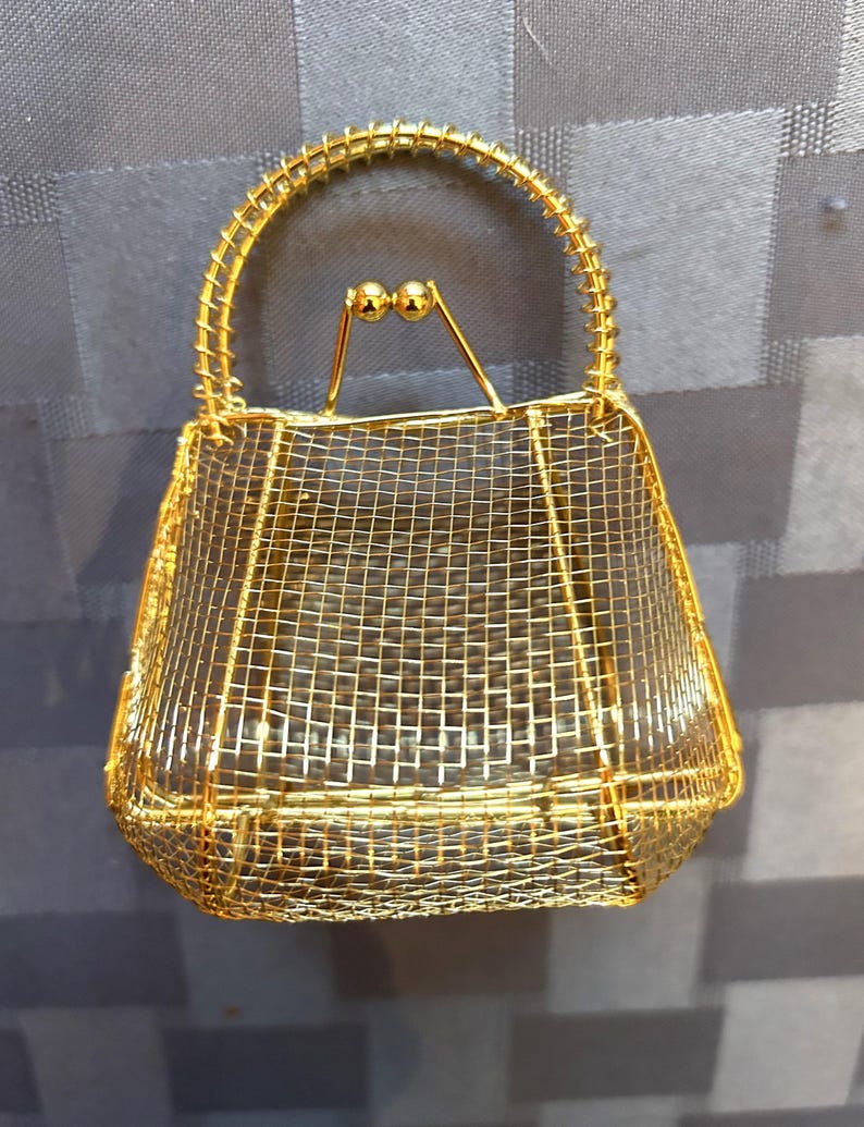 May include: A gold wire mesh handbag with a wire handle and two gold ball accents.