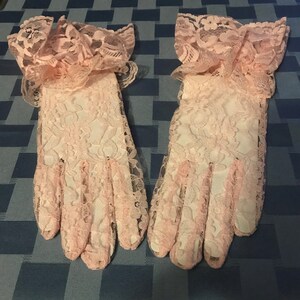 May include: A pair of pink lace gloves with ruffled cuffs. The gloves are made of delicate lace and have a soft, feminine look.
