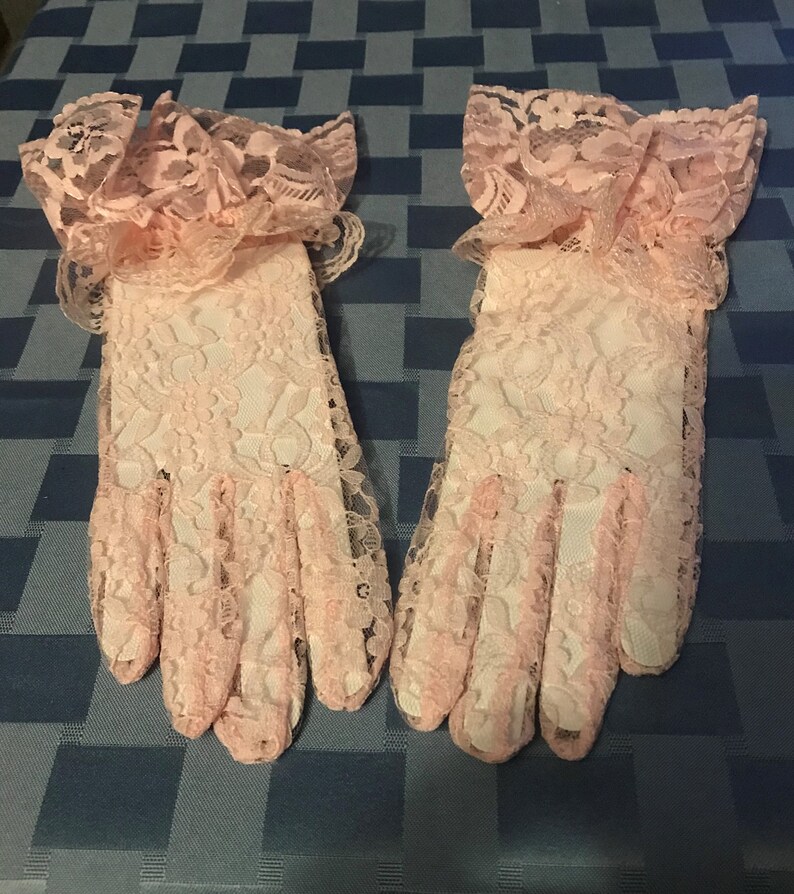May include: A pair of pink lace gloves with ruffled cuffs. The gloves are made of delicate lace and have a soft, feminine look.