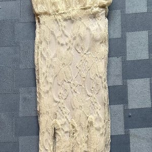 May include: A pair of ivory lace gloves with a delicate floral pattern. The gloves have a ruffled cuff and are made of a sheer fabric.