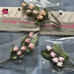 May include: Three packages of artificial flower sprays, each with a different color. The packages are labeled "Lasting Keepsake" and include the product name, color, and number of stems. The colors are mauve, light orchid, and white.