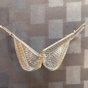 May include: A silver wire mesh basket with a heart shape. The basket is open and the two sides are folded back.