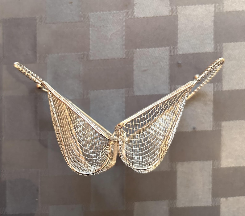 May include: A silver wire mesh basket with a heart shape. The basket is open and the two sides are folded back.