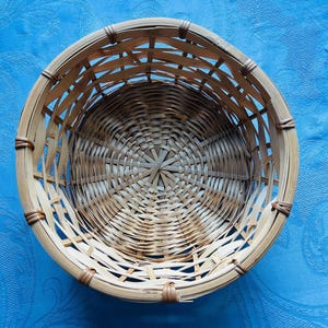 Puede incluir: Una cesta redonda de tejido abierto construida con tiras de bamb&uacute; natural de color marr&oacute;n claro. La cesta presenta una base circular con un patr&oacute;n de tejido radiante y lados verticales reforzados con una fina uni&oacute;n marr&oacute;n oscura.