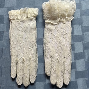 May include: A pair of white lace gloves with a frilled edge. The gloves are made of delicate lace and have a classic design.