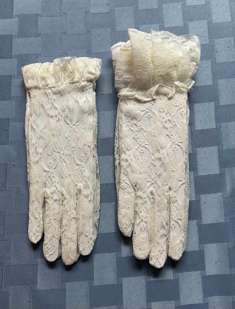 May include: A pair of white lace gloves with a frilled edge. The gloves are made of delicate lace and have a classic design.