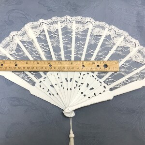 May include: White lace folding fan with a white handle and a tassel. The fan is 12 inches wide.