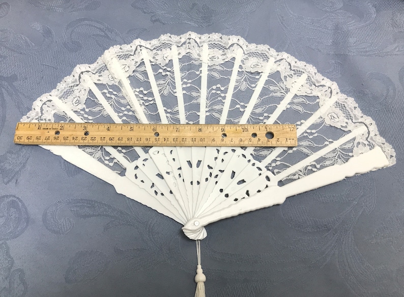 May include: White lace folding fan with a white handle and a tassel. The fan is 12 inches wide.