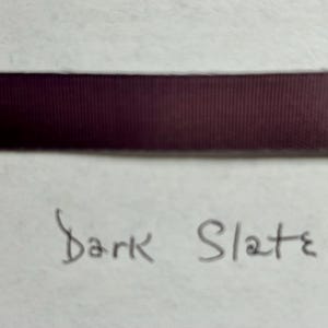 May include: A horizontal strip of dark purple ribbon with a fine ribbed texture. Below the ribbon, the words Dark Slate are handwritten in black ink on a light-colored surface. The ribbon has a smooth, matte finish and consistent color.