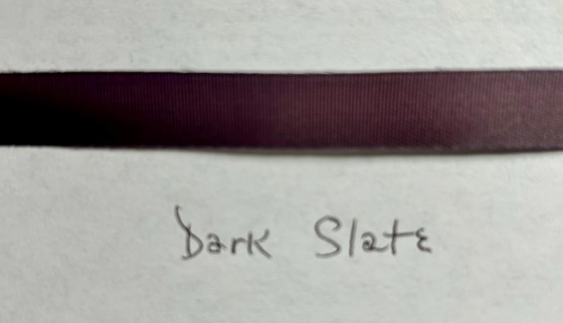 May include: A horizontal strip of dark purple ribbon with a fine ribbed texture. Below the ribbon, the words Dark Slate are handwritten in black ink on a light-colored surface. The ribbon has a smooth, matte finish and consistent color.