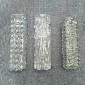 May include: Three clear glass vases with textured designs. The vase on the left has a bubble pattern, the middle vase has a bark-like texture, and the right vase has a diamond pattern. The vases are cylindrical and of varying heights.