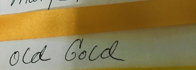 May include: A horizontal strip of smooth, shiny gold ribbon positioned across a white surface. Below the ribbon, the words "old Gold" are written in black cursive script. The ribbon has a consistent texture and a vibrant, reflective yellow-gold color.