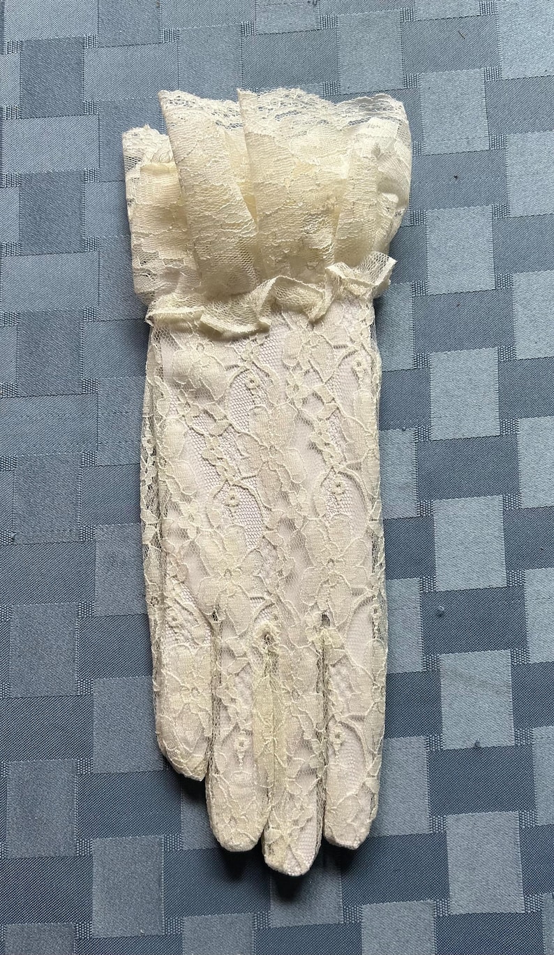 May include: A pair of white lace gloves with a ruffled cuff. The gloves are made of delicate lace and have a classic design.