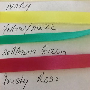 May include: Four horizontal strips of smooth satin ribbon in ivory, yellow, seafoam green, and dusty rose colors. Each ribbon is labeled with handwritten text below it, reading ivory, yellow/maize, seafoam green, and dusty rose respectively.