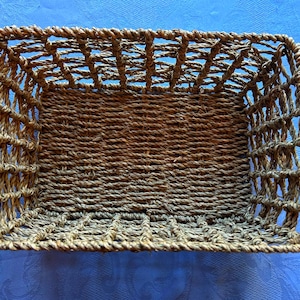 May include: A rectangular woven basket with a natural brown color. The basket has a lattice-like pattern on the sides and a tightly woven base. The basket is made of a natural fiber material.